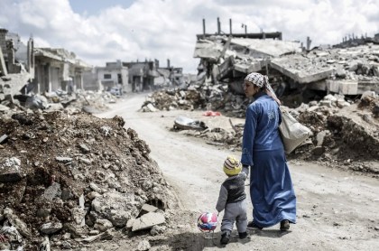 TOPSHOTS A Kurdish Syrian woman walks with her child past the ruins of the town of Kobane, also known as Ain al-Arab, on March 25, 2015. Islamic State (IS) fighters were driven out of Kobane on January 26 by Kurdish and allied forces. AFP PHOTO/YASIN AKGUL